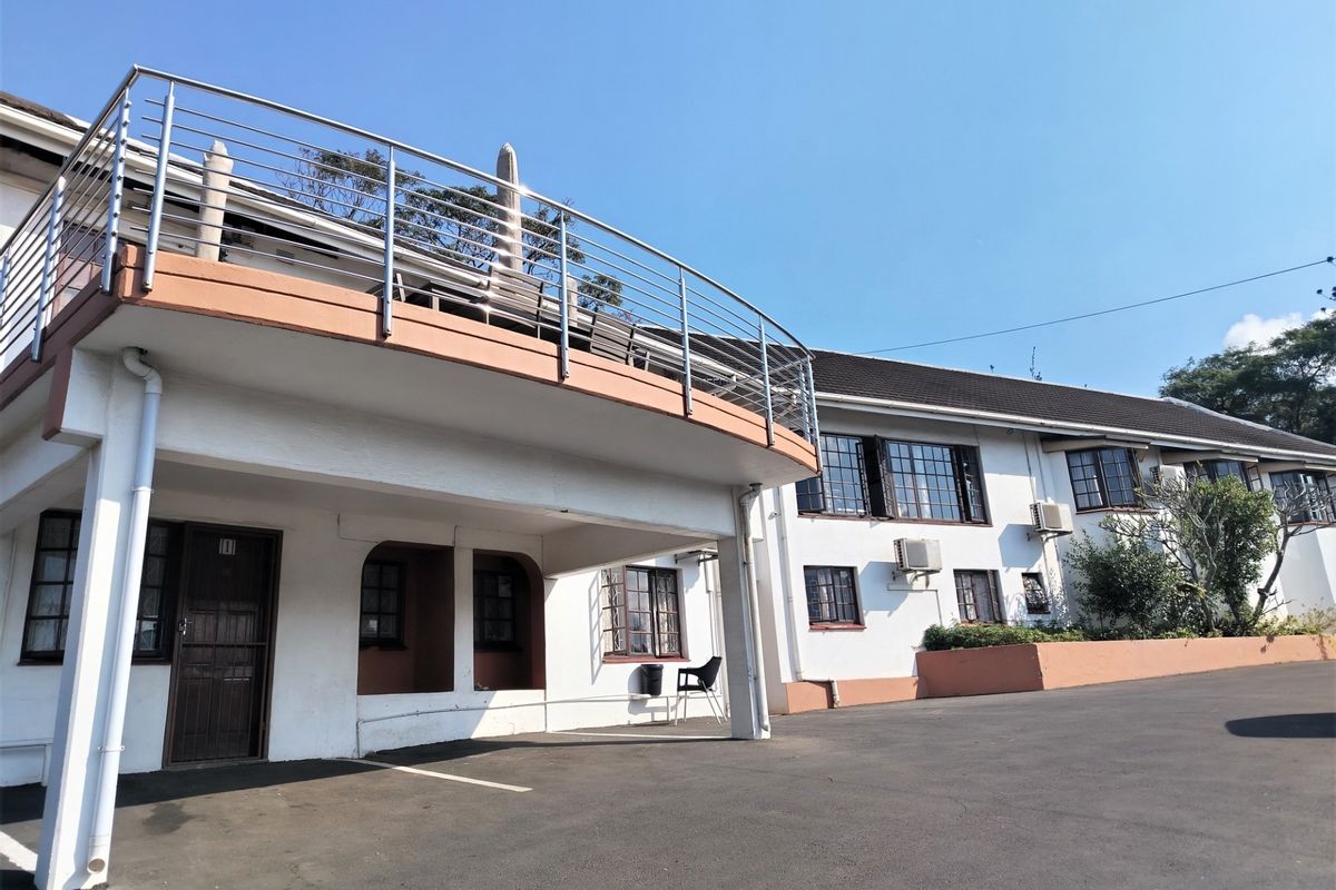 Exterior view of the lodge featuring a large elevated balcony with stainless steel railings, asphalt driveway, and white facade with casement windows.