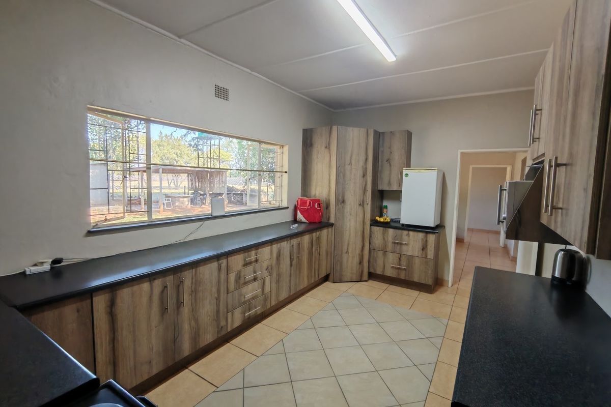 A functional kitchen featuring wood-look cabinetry, dark countertops, tiled flooring, and a large window providing natural light and views of the property grounds.