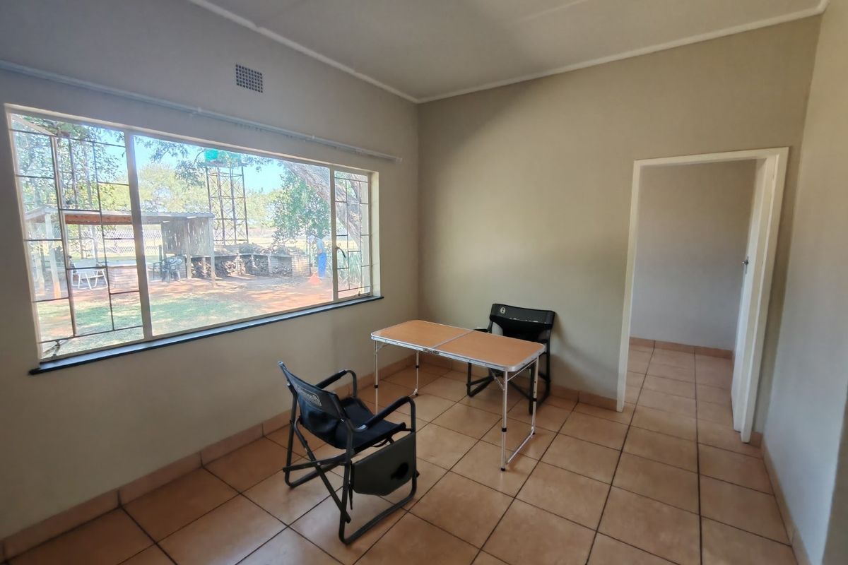 A simple, neutrally painted room featuring large windows with security bars, tiled flooring, and a doorway leading to an adjacent space.