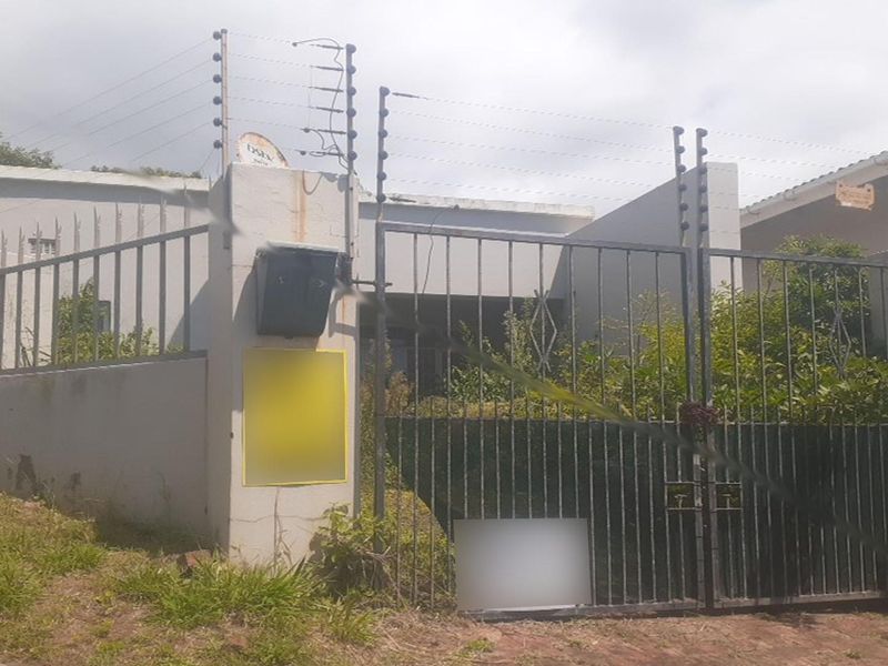 Front view of the property featuring a metal security gate, perimeter wall, and installed electric fencing.
