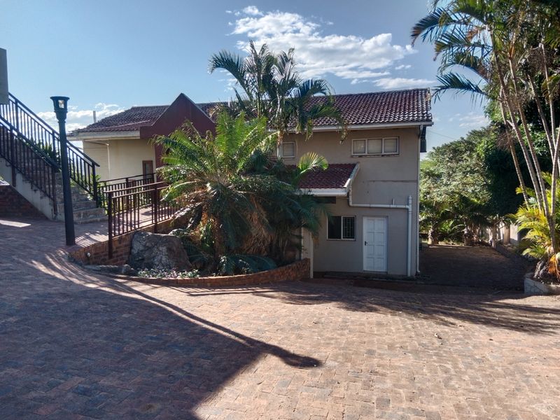 Exterior view of a multi-level residential property featuring a paved driveway, external staircase, and established garden landscaping.