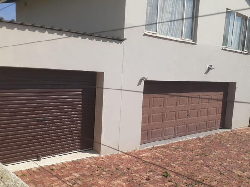 Exterior view of a double garage with brown sectional doors, brick paved driveway, and external wall-mounted lighting.