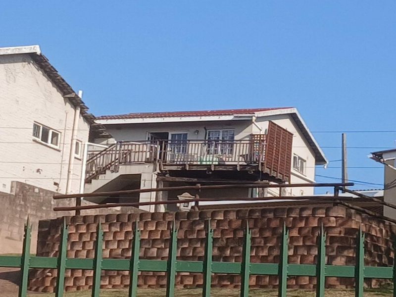 Exterior view of a residential property featuring a raised timber deck, retaining wall, and metal perimeter fencing.