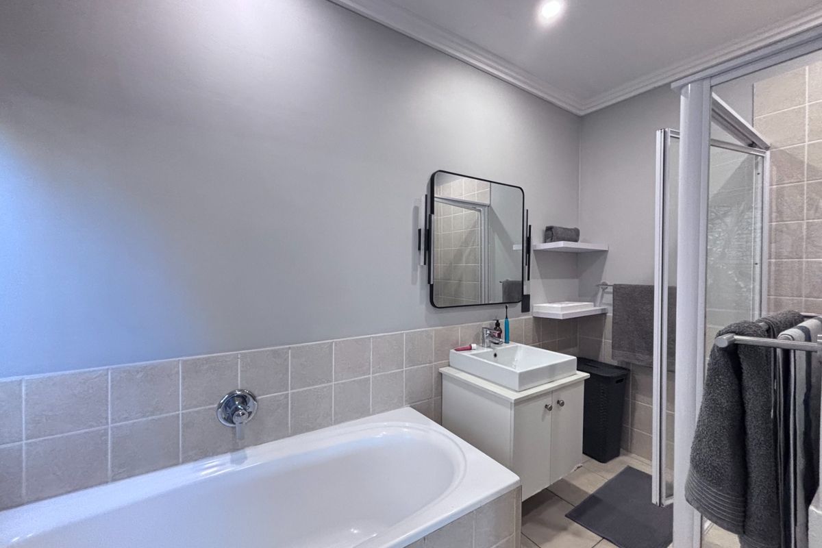Modern bathroom featuring a built-in bathtub, a vanity with a basin, a wall-mounted mirror, and a separate glass-enclosed shower area.
