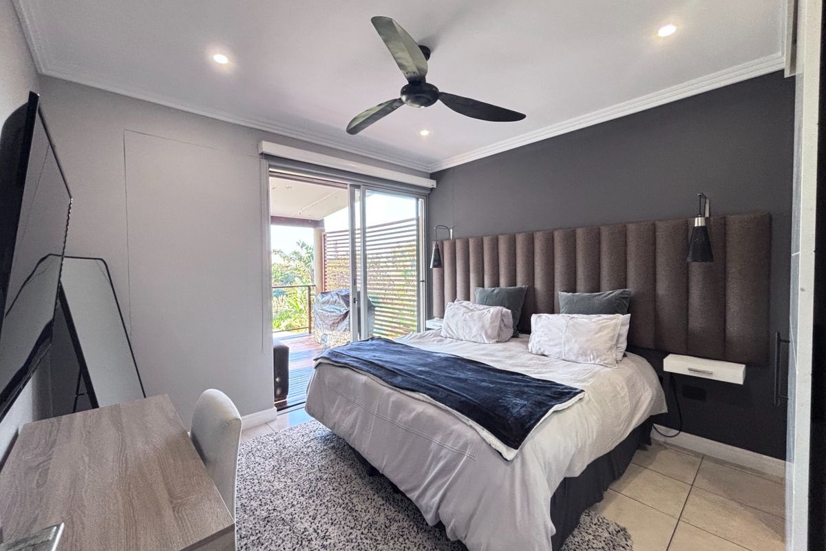 A well-maintained bedroom featuring a built-in upholstered headboard, ceiling fan, recessed lighting, and sliding glass doors leading to a private balcony.