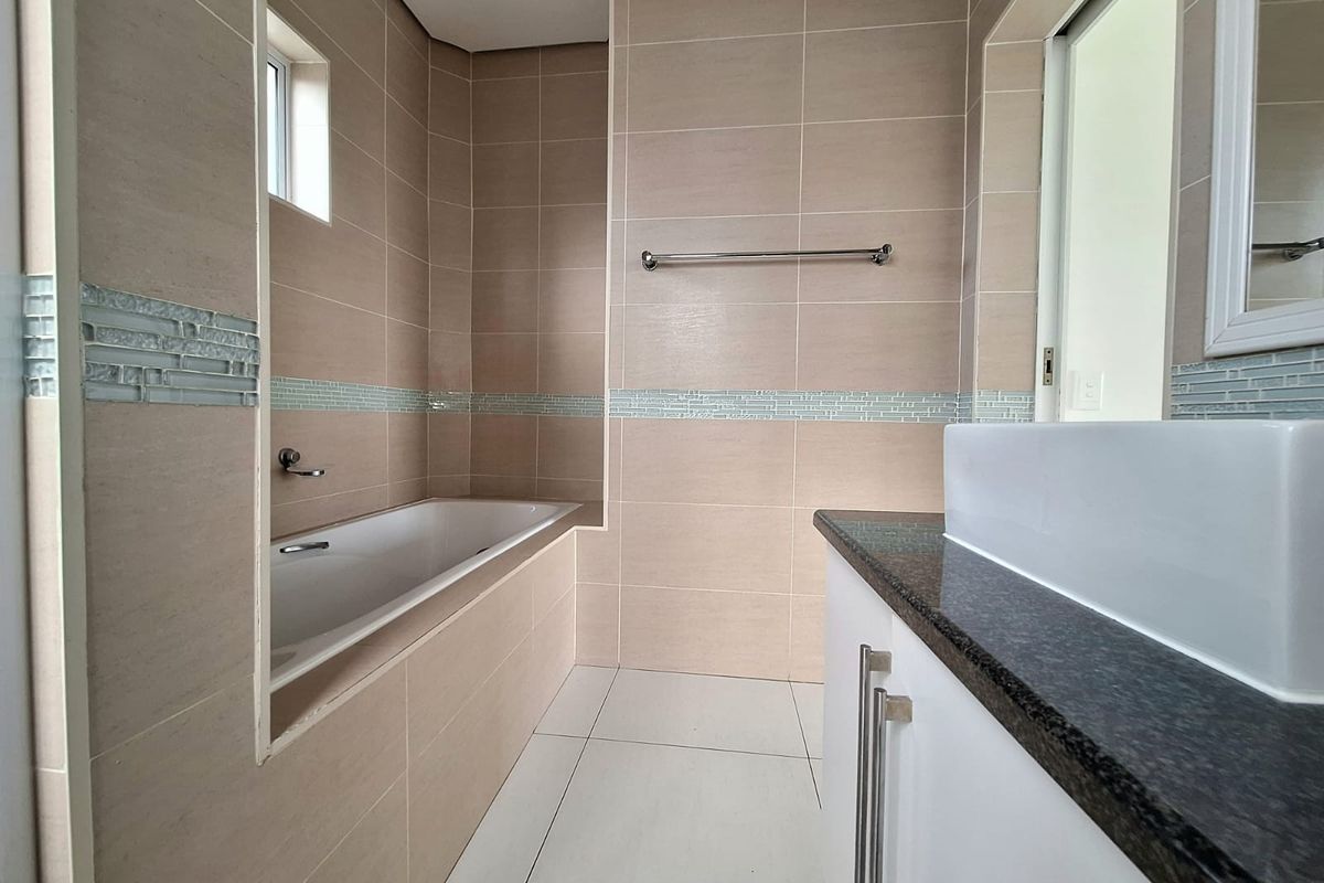 A modern bathroom featuring neutral wall tiling, a built-in bathtub, a granite-topped vanity with a vessel sink, and a chrome towel rail.