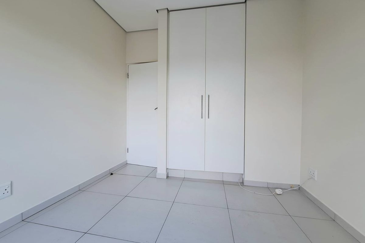 A clean, empty bedroom featuring neutral tiled flooring, built-in white cabinetry, and a standard interior door.