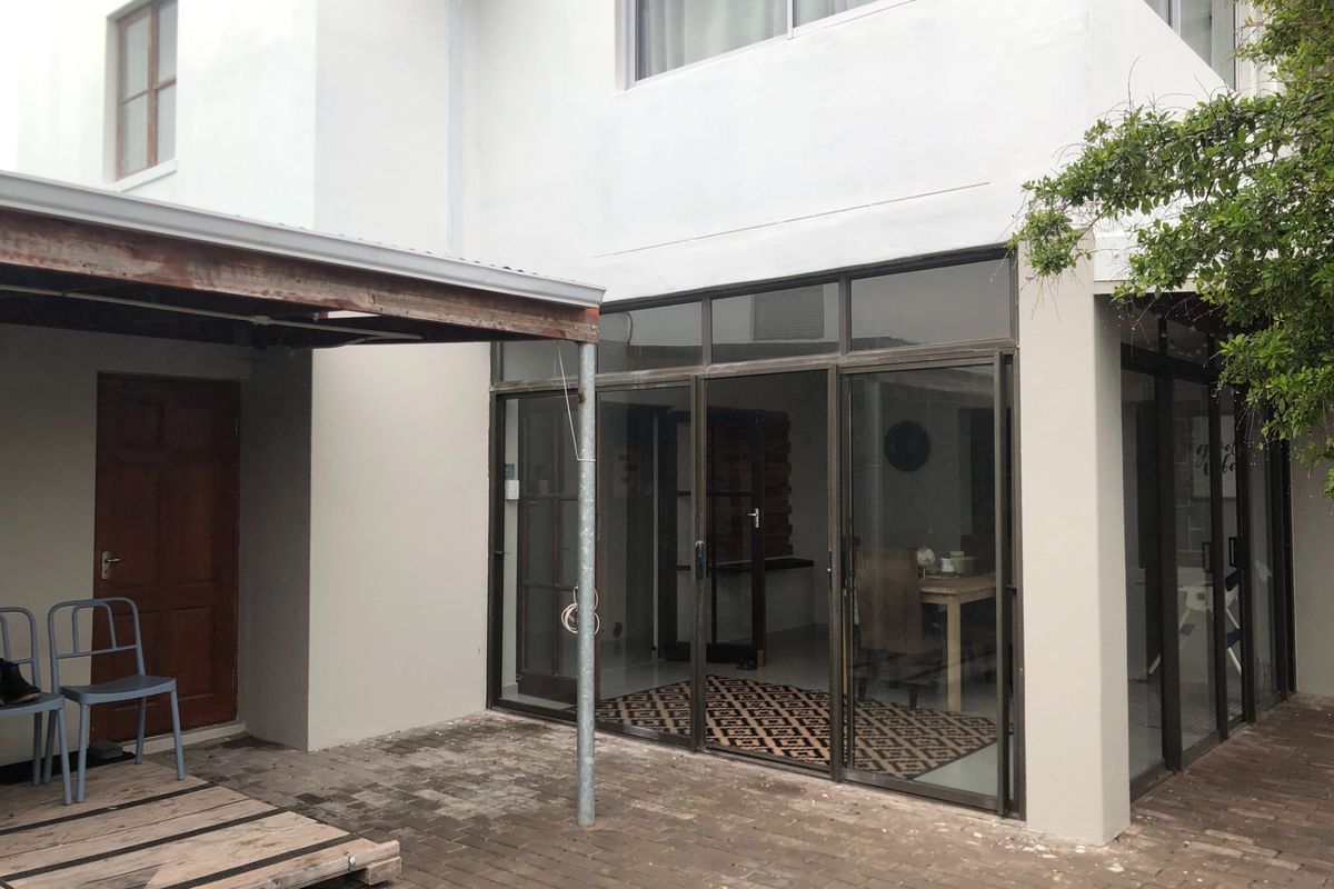 Rear exterior view featuring a paved patio area, covered pergola structure, and large aluminium sliding doors providing access to the interior living space.