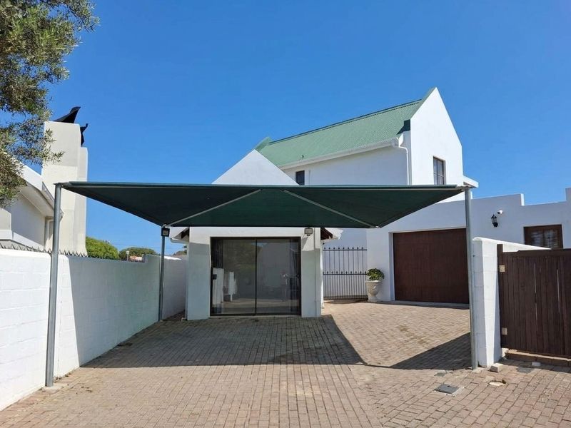 Front exterior view of the property featuring a paved driveway, a shade sail carport, and a white facade with a garage and sliding door entrance.