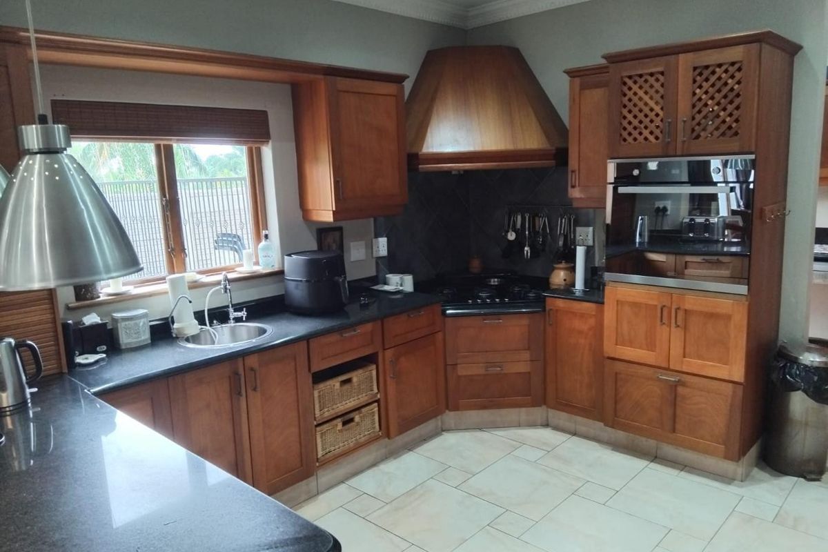 A traditional kitchen featuring wooden cabinetry, dark granite countertops, a built-in oven, and a corner hob with a wooden extractor hood.