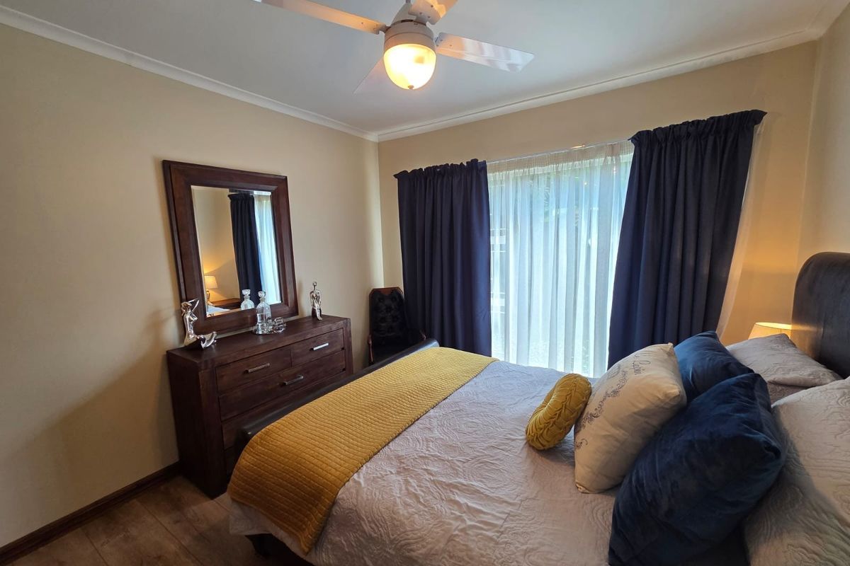 A well-maintained bedroom featuring a ceiling fan, wood-look flooring, and large window with curtains, providing a comfortable and functional living space.