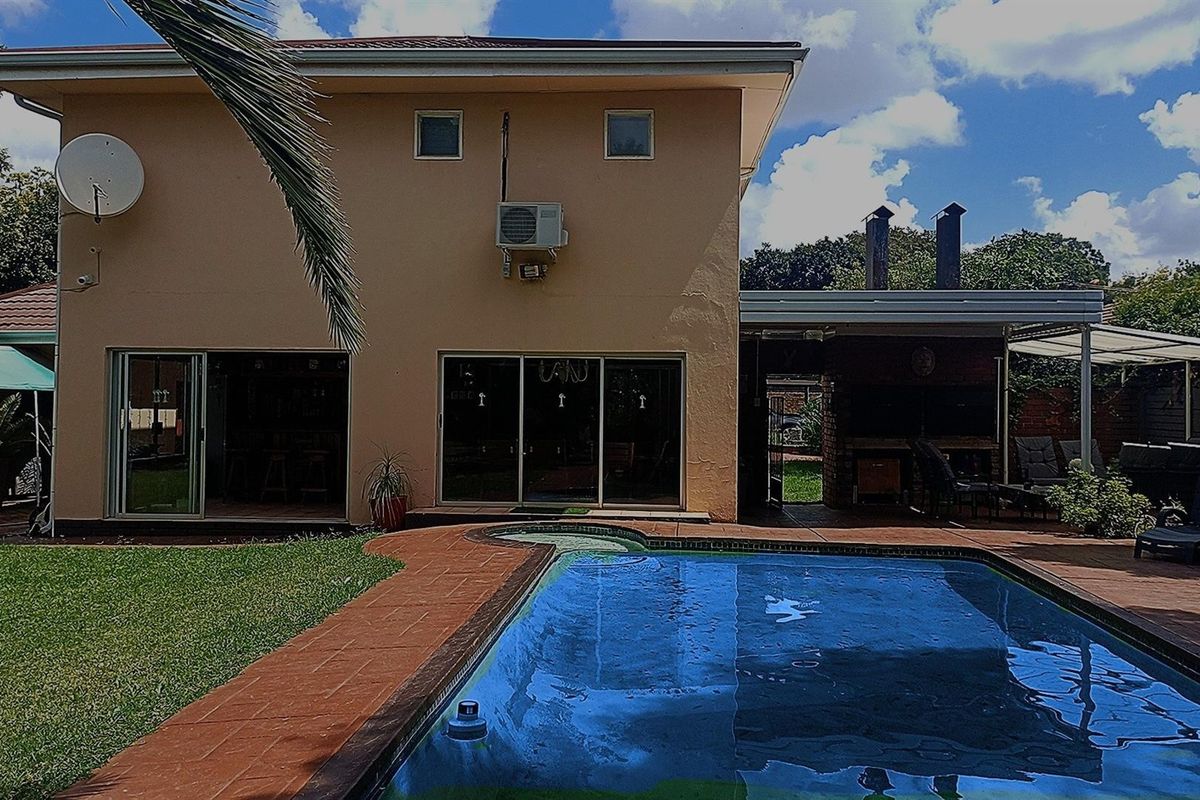 Rear view of the house featuring a swimming pool, paved patio area, built-in braai, and sliding door access to the interior living spaces.