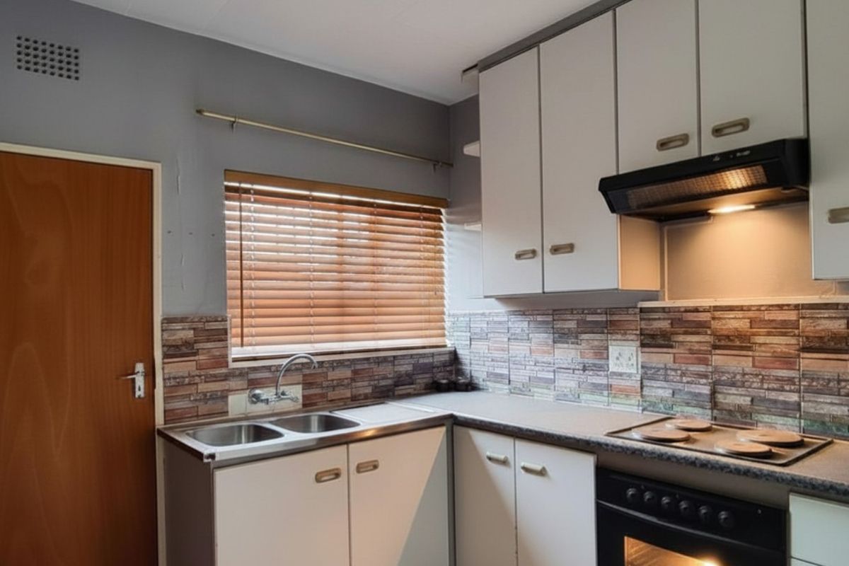 A functional kitchen featuring built-in cabinetry, a stainless steel double sink, integrated oven, and hob with an extractor fan.