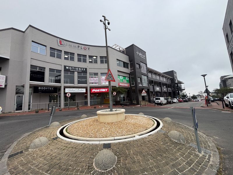 Exterior view of a multi-story commercial retail complex featuring various business signage and a central paved roundabout.