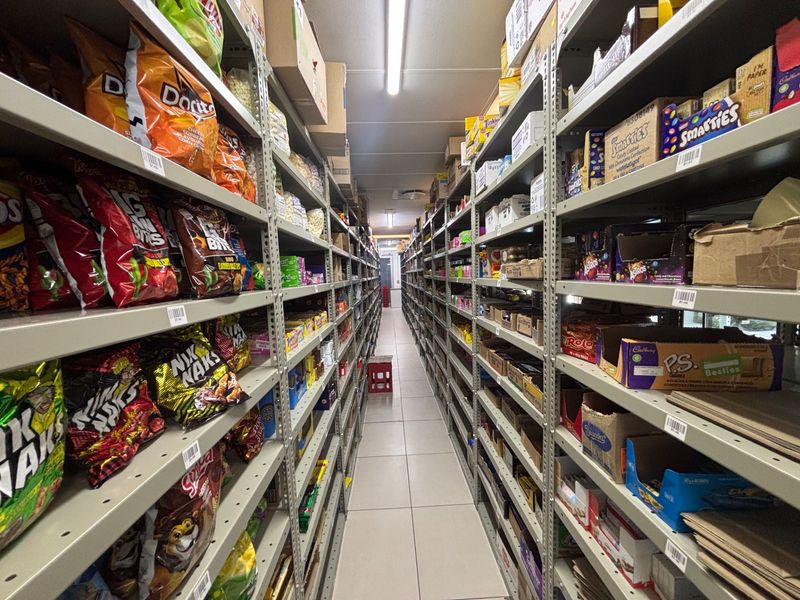 A well-organized retail storage aisle featuring extensive industrial metal shelving units and bright overhead fluorescent lighting.