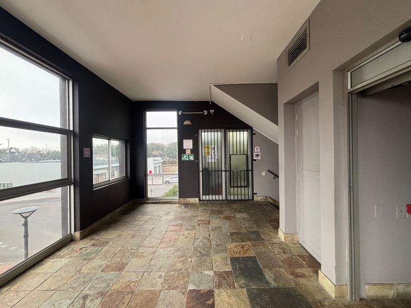 A spacious commercial entry foyer featuring large windows, stone tile flooring, and secure access points, providing a professional and well-lit reception area.