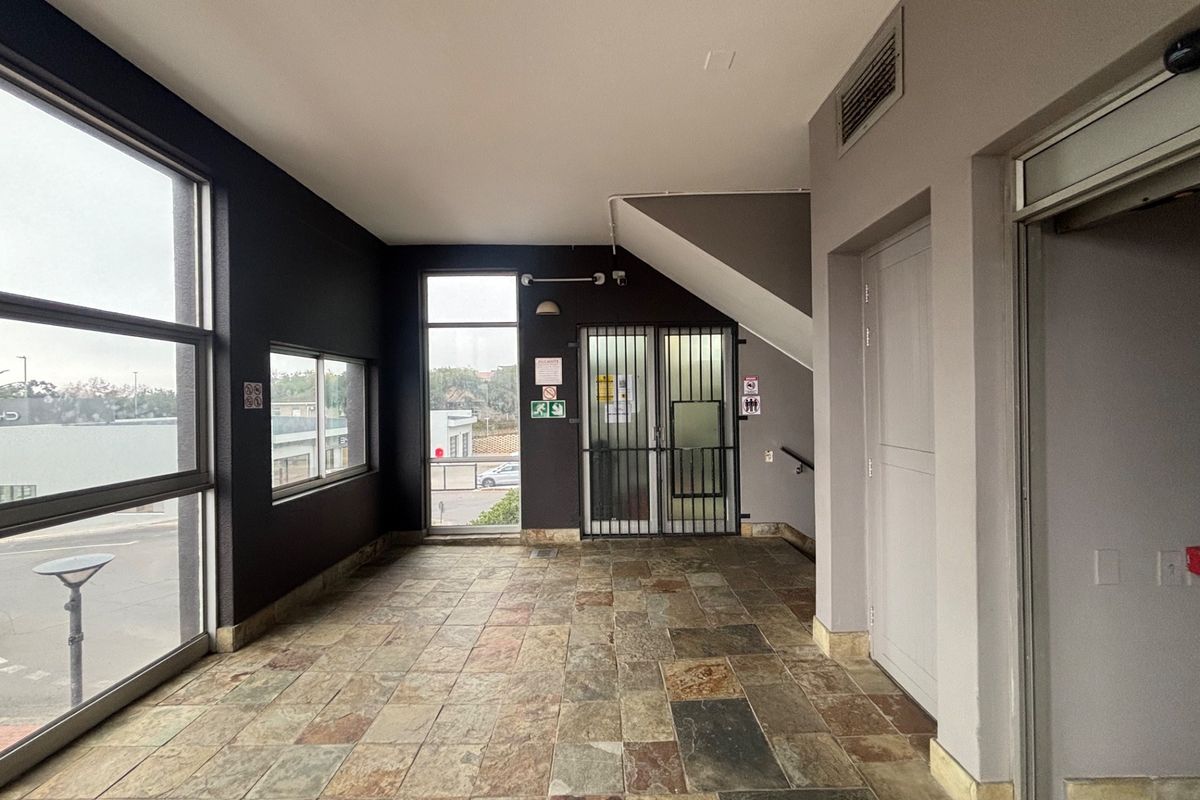 A spacious commercial entry foyer featuring large windows, stone tile flooring, and secure access points, providing a professional and well-lit reception area.