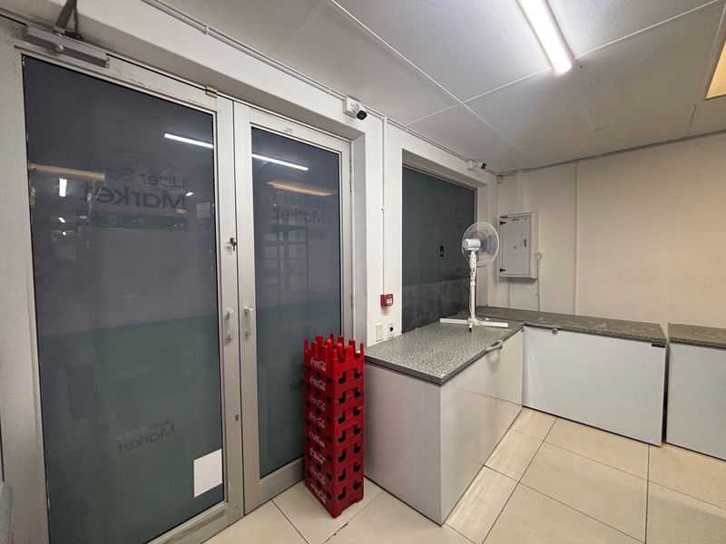 A functional utility or service area featuring tiled flooring, built-in counter space, and secure glass entry doors, suitable for retail operations.