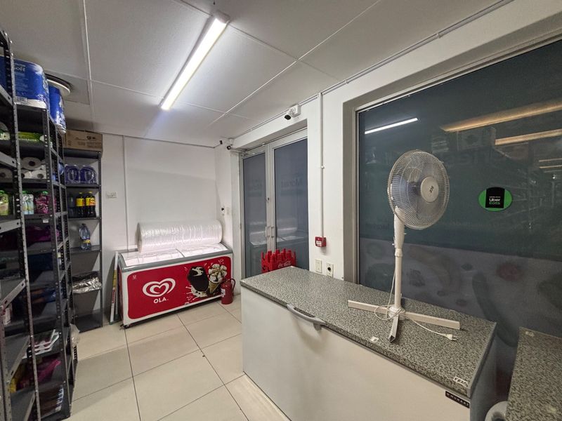 A functional retail utility or storage area featuring tiled flooring, fluorescent lighting, and a glass entrance door.