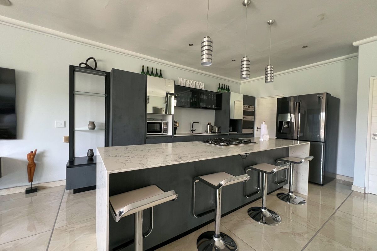 Modern kitchen featuring a large central island with stone countertop, integrated gas hob, dark cabinetry, and sleek pendant lighting.