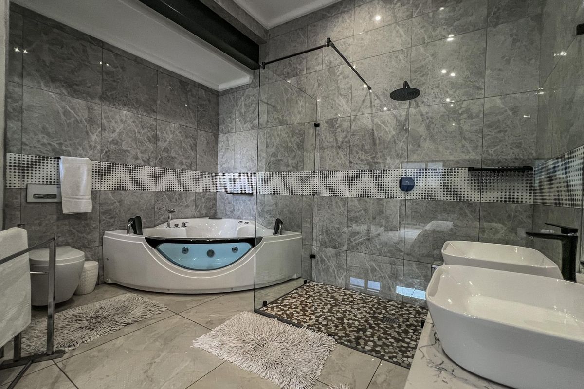 Modern bathroom featuring a corner spa bathtub, a glass-enclosed walk-in shower with pebble flooring, and dual vessel sinks on a marble-topped vanity.