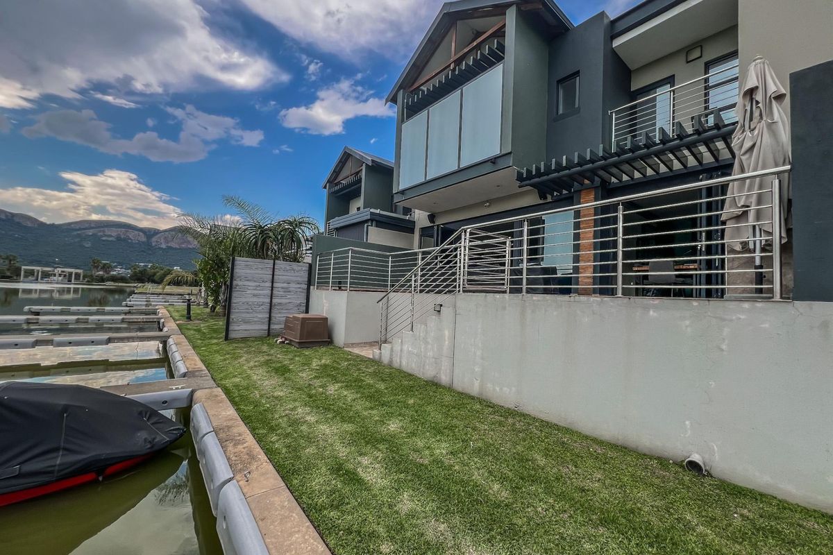 Rear view of a modern multi-story waterfront property featuring a private lawn, stainless steel balustrades, and direct access to a boat mooring.