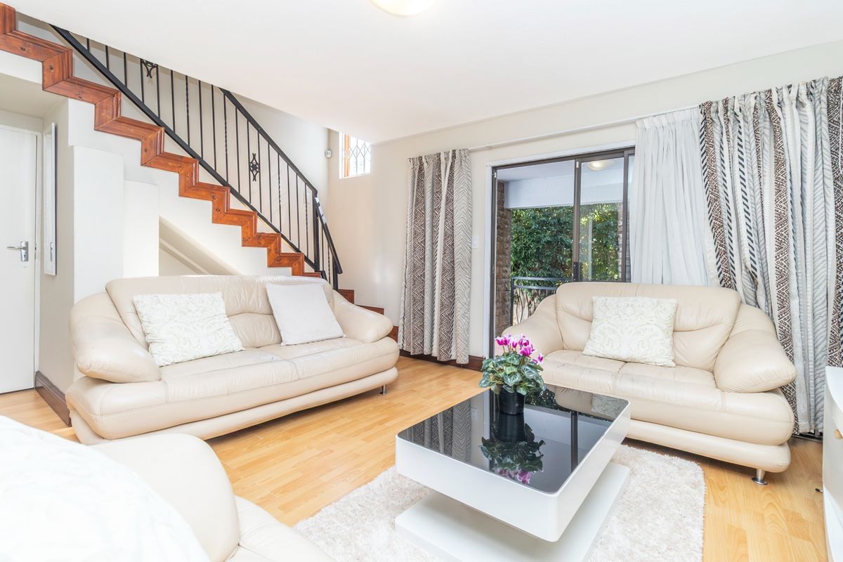 A bright living room featuring light wood flooring, a staircase with a wrought iron railing, and sliding glass doors leading to an outdoor area.