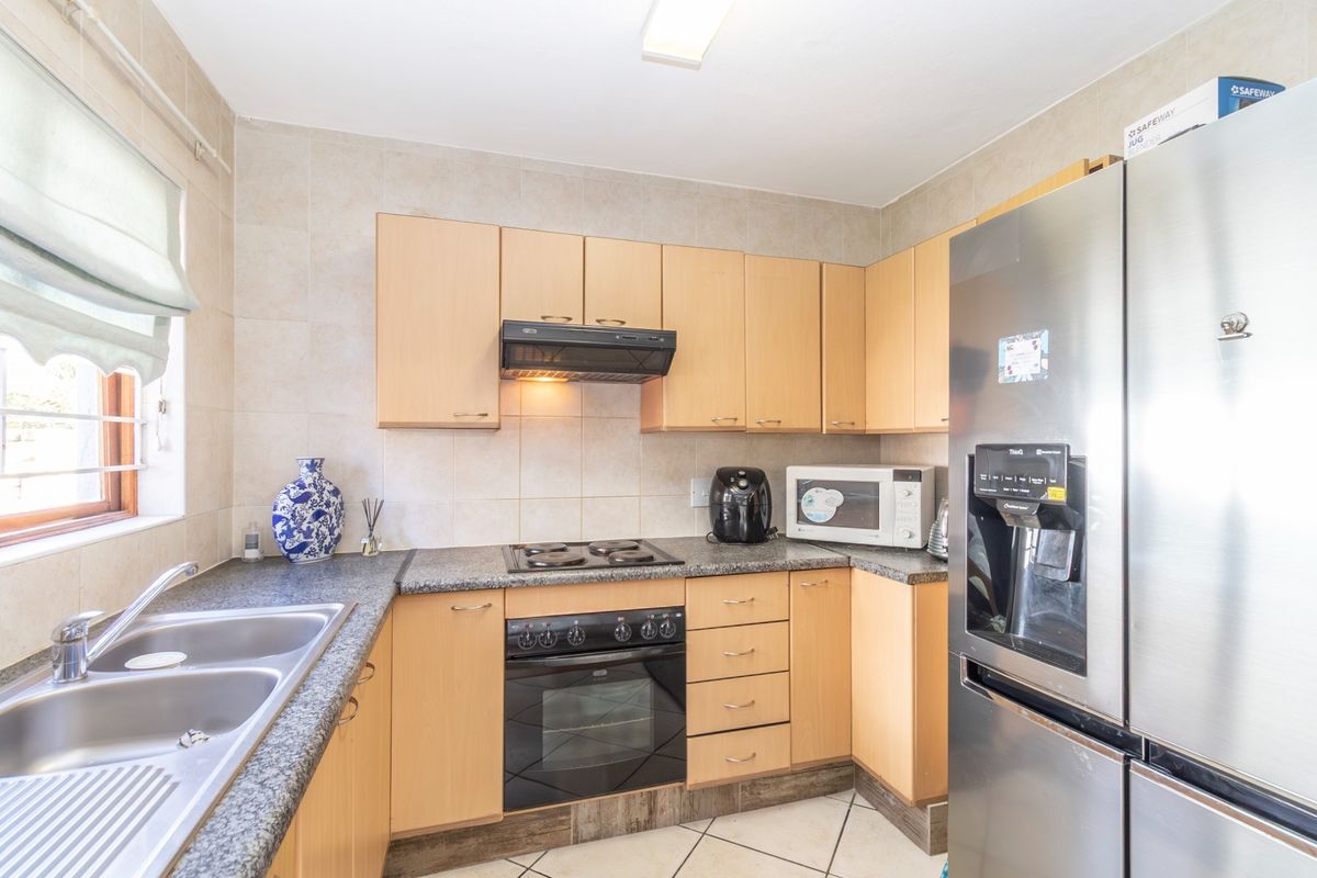 A functional kitchen featuring light wood cabinetry, granite countertops, a built-in oven with hob, extractor fan, and a double stainless steel sink.