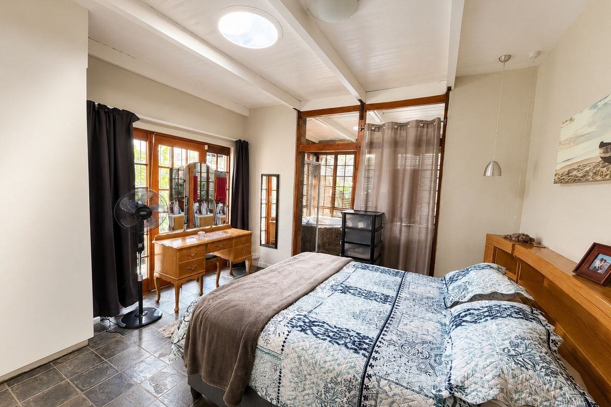 A bedroom featuring exposed beam ceilings, a skylight, tiled flooring, and direct access to an adjoining space through timber-framed glass doors.