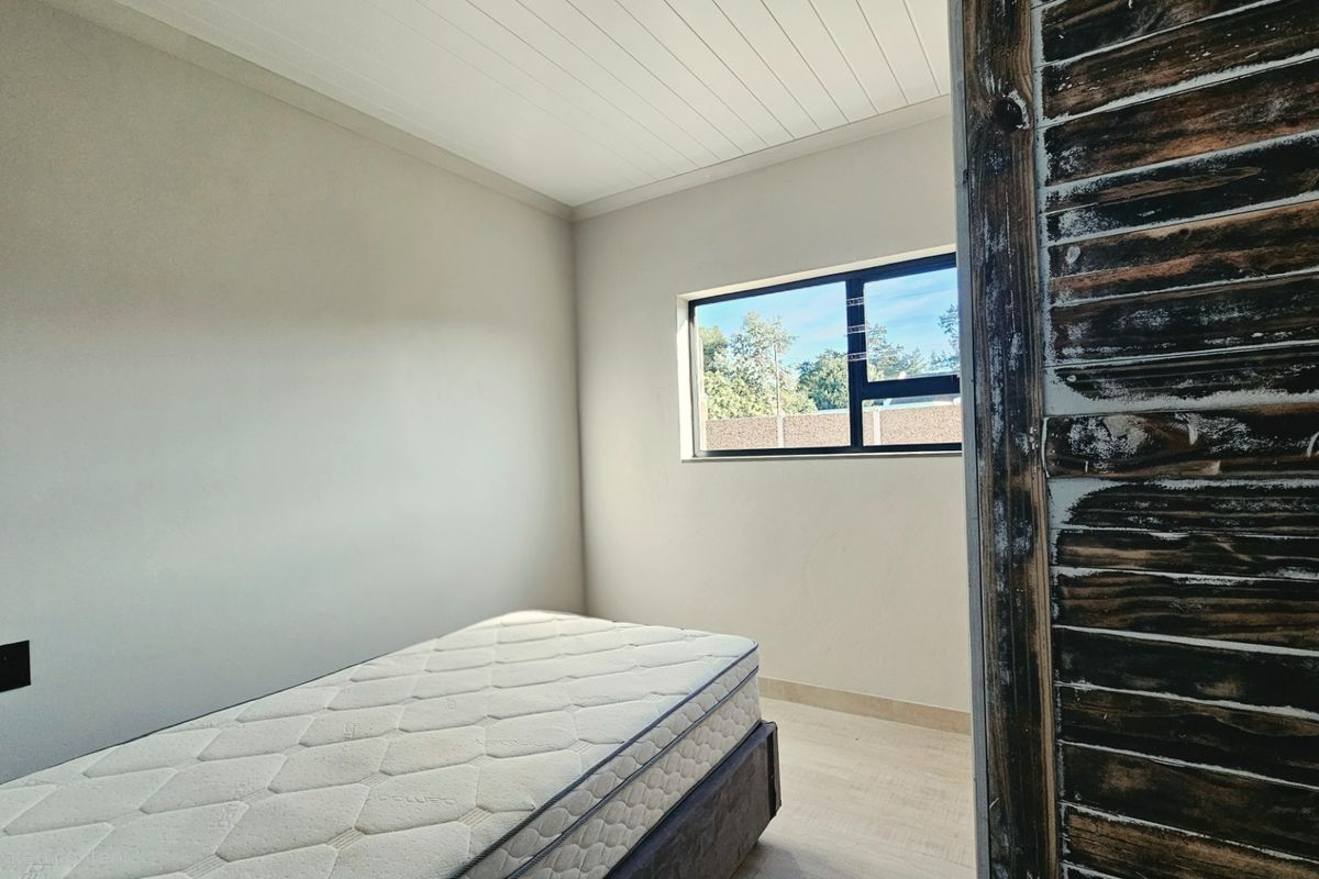 A simple bedroom featuring light-toned flooring, a white paneled ceiling, and a window with a view of the exterior.