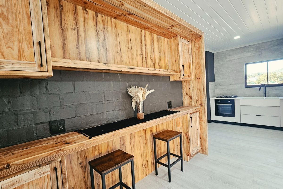 Modern kitchen featuring custom timber cabinetry, a dark brick feature wall, integrated breakfast bar, and built-in oven with gas cooktop.