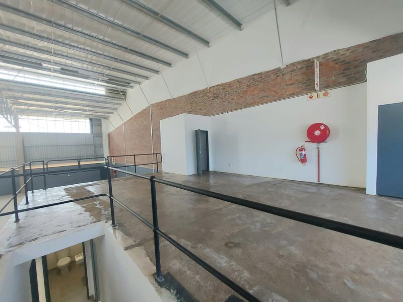Spacious industrial mezzanine level featuring exposed brickwork, concrete flooring, and integrated fire safety equipment, suitable for storage or office conversion.