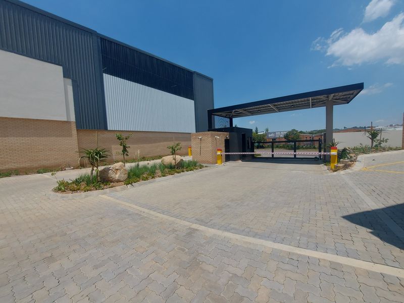 Industrial property entrance featuring a paved driveway, security boom gate, and a modern guard house with metal and brick facade finishes.