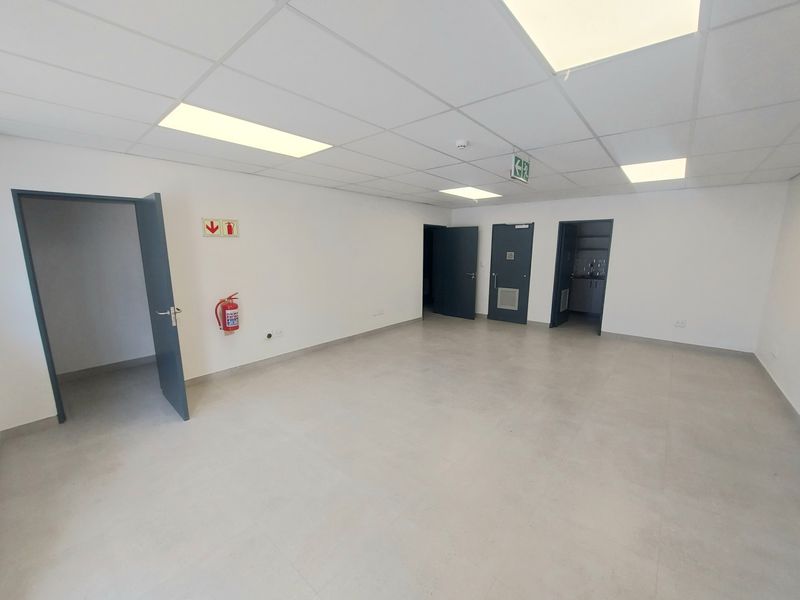 A clean, vacant industrial office space featuring neutral tiled flooring, a suspended ceiling with recessed lighting, and multiple access doors.