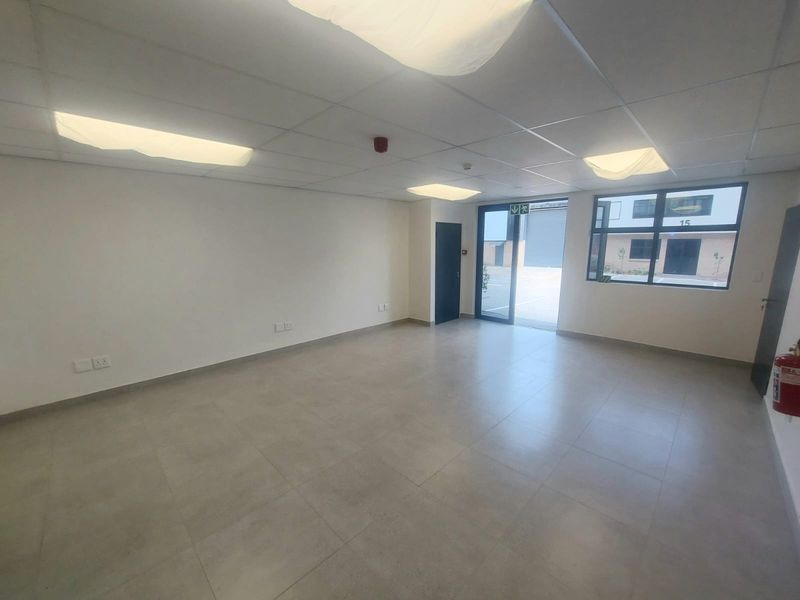 A clean, modern, and empty office space featuring tiled flooring, a suspended ceiling with recessed lighting, and large windows providing natural light.