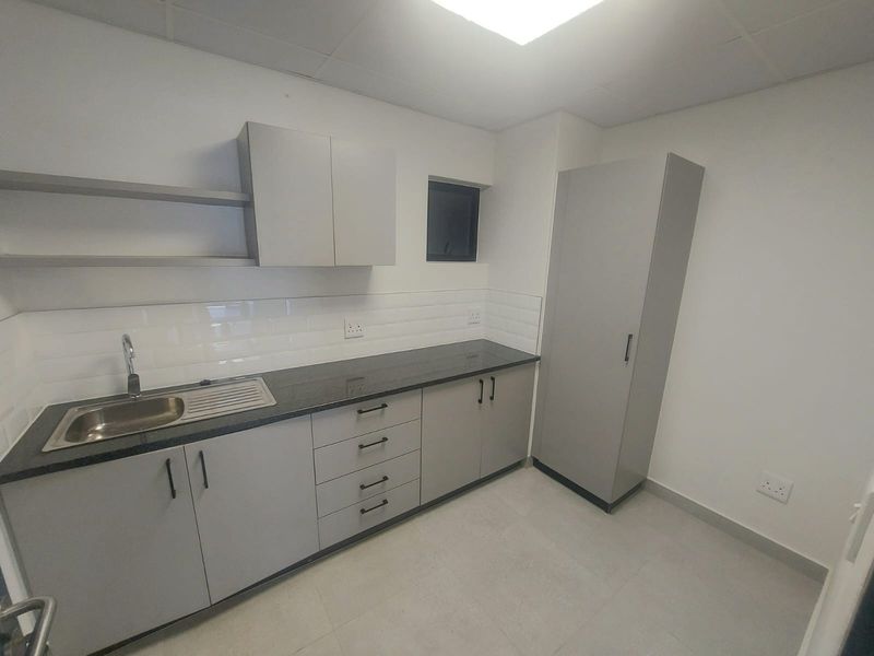 A clean, modern kitchenette featuring grey built-in cabinetry, granite countertops, a stainless steel sink, and a subway tile backsplash.