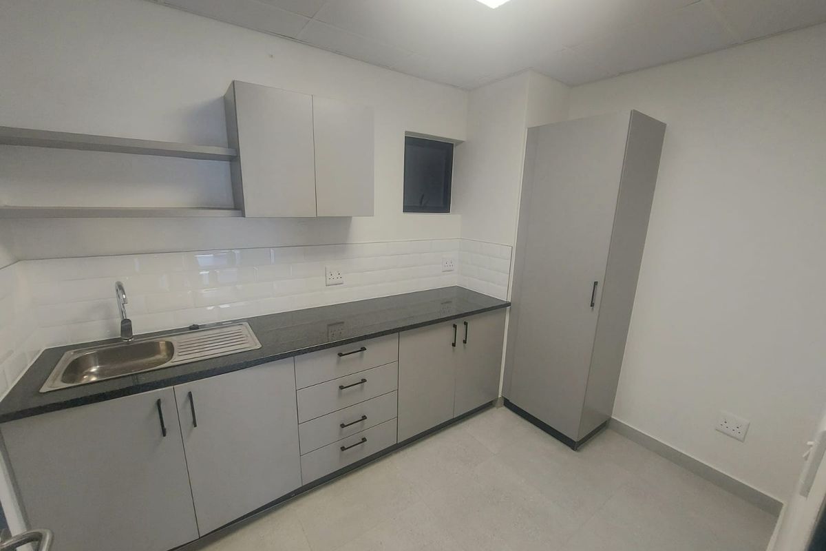 A clean, modern kitchenette featuring grey built-in cabinetry, granite countertops, a stainless steel sink, and a subway tile backsplash.