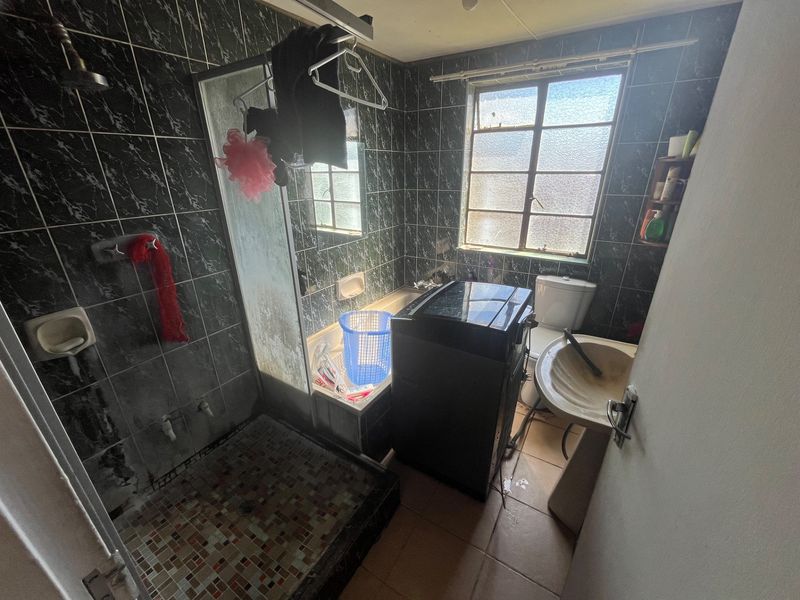 A compact bathroom featuring a shower enclosure, pedestal basin, and toilet, finished with dark marble-effect wall tiles and a window for natural light.
