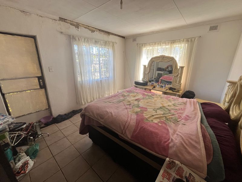A bedroom featuring tiled flooring and direct exterior access, currently requiring significant maintenance and cosmetic repairs to the walls and ceiling.