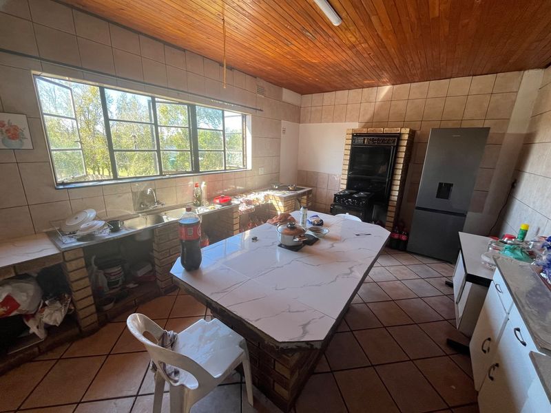 A dated kitchen featuring brick-built cabinetry, a central island, tiled flooring, and a timber-paneled ceiling with large windows providing natural light.