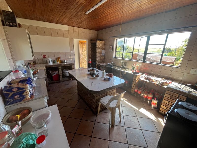 A dated kitchen featuring brick-built cabinetry, a central island, tiled flooring, and a timber-clad ceiling with large windows providing natural light.