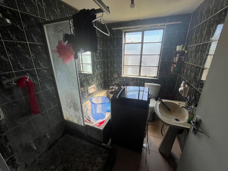 A dated bathroom featuring a pedestal basin, toilet, and a combined shower and bathtub area with dark marble-effect wall tiles.