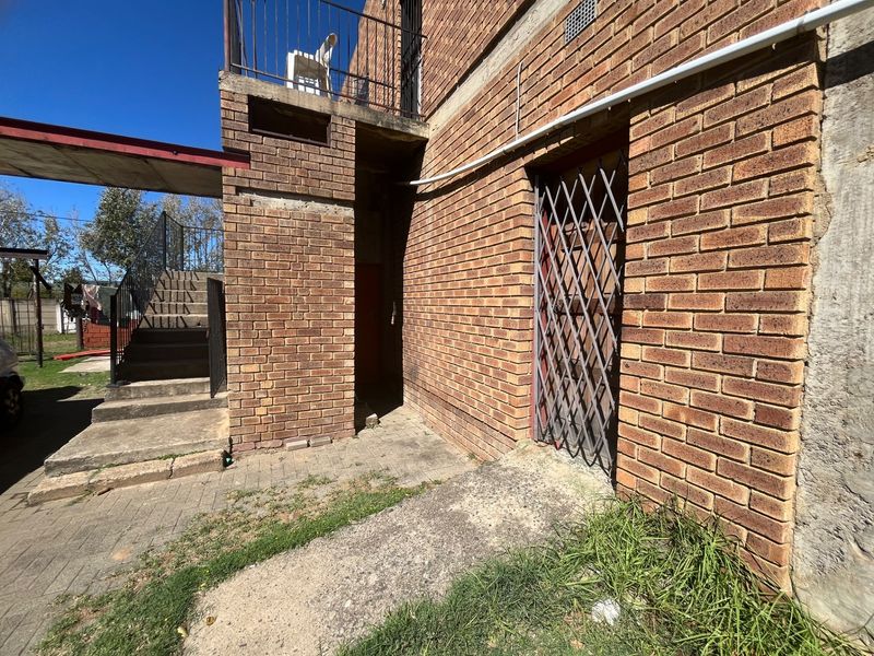 Exterior view of a brick building featuring a concrete staircase, metal security gate, and paved walkway area requiring maintenance.