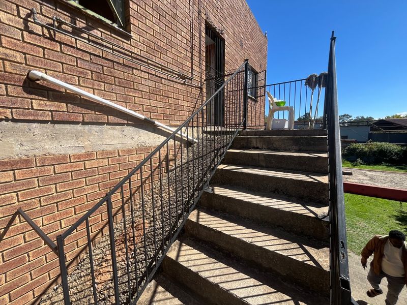 Exterior view of a brick house featuring a concrete staircase with metal railings leading to an elevated entrance.