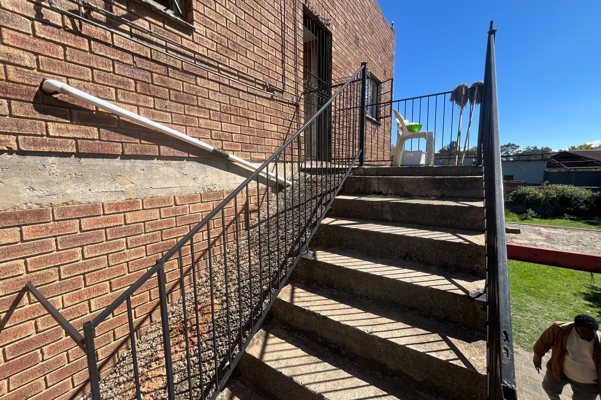 Exterior view of a brick house featuring a concrete staircase with metal railings leading to an elevated entrance.