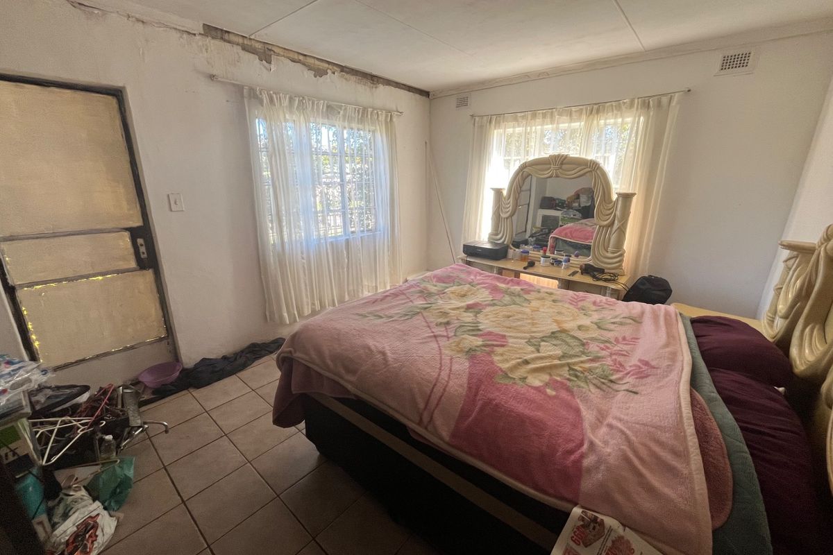 A bedroom featuring tiled flooring and direct exterior access, currently requiring significant maintenance and cosmetic repairs to the walls and ceiling.
