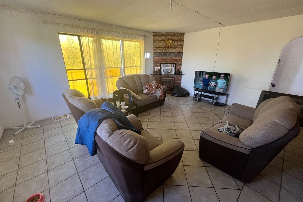 A living room featuring tiled flooring and a brick fireplace surround, offering a functional space with natural light from large windows.