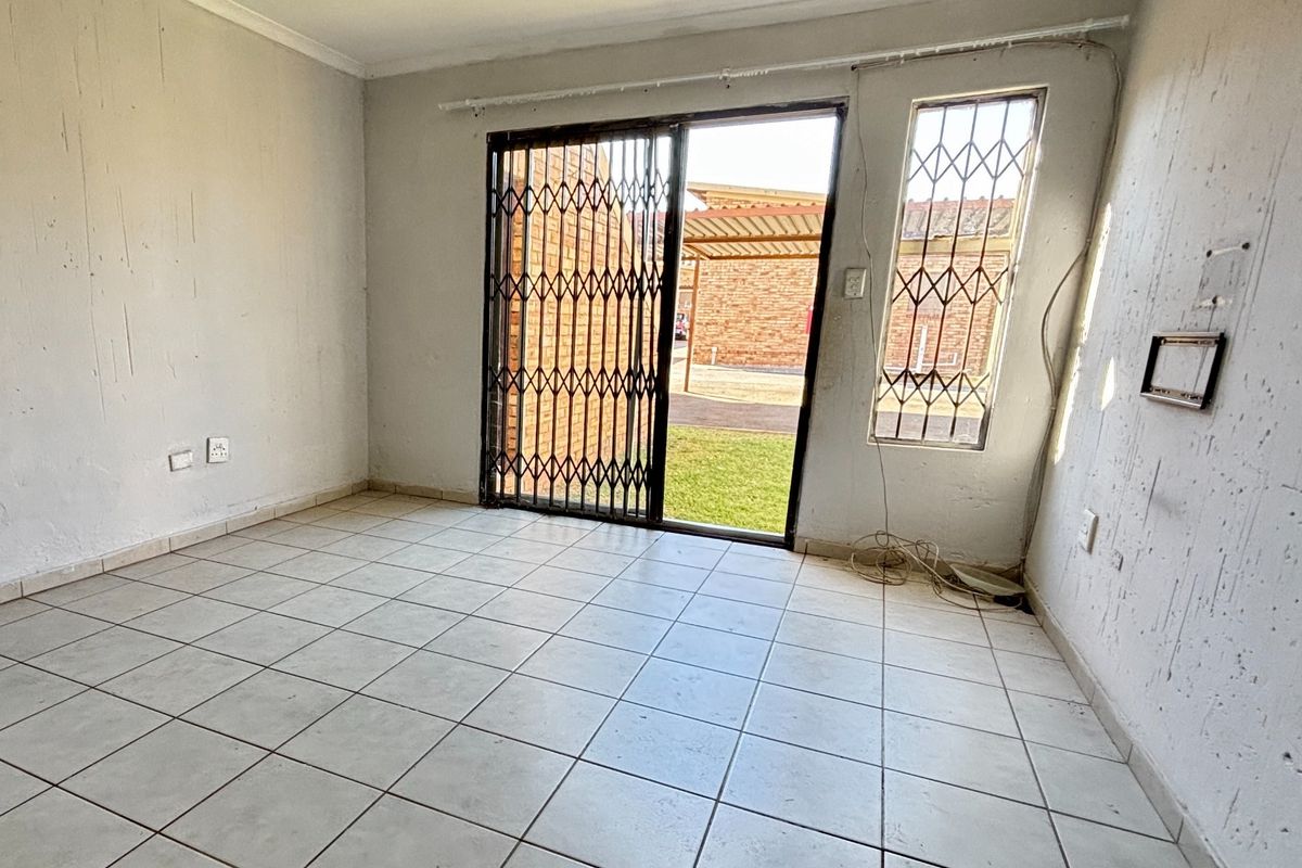 An empty living room featuring tiled flooring, a sliding glass door with security gate, and access to an outdoor area.