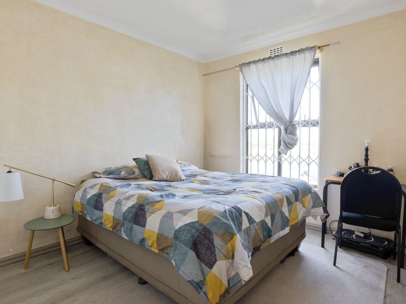 A bedroom featuring light-toned walls, wood-look flooring, and a window fitted with security bars and a curtain rod.