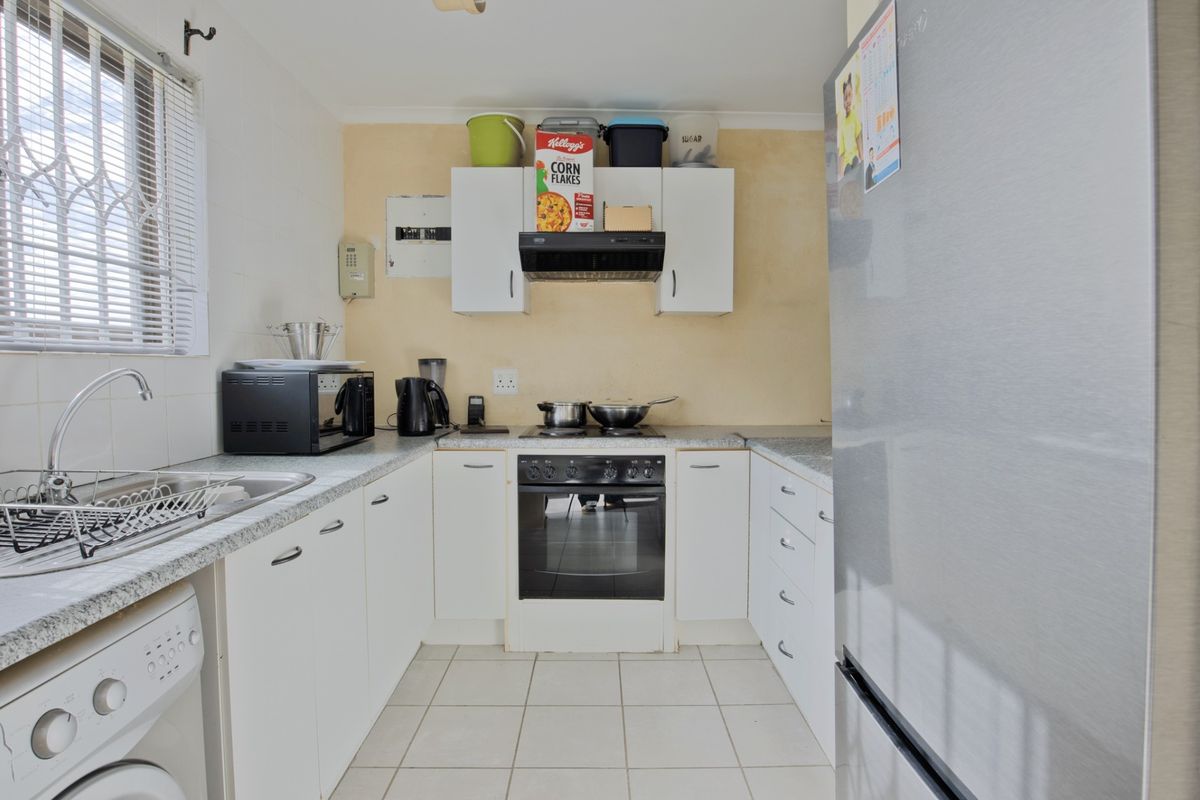 Compact kitchen featuring white cabinetry, laminate countertops, built-in oven with extractor fan, and tiled flooring with integrated laundry plumbing.
